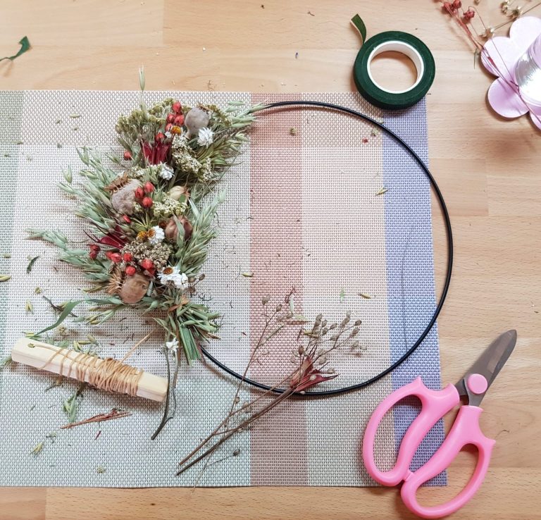 Ein Kranz aus Trockenblumen, Draht und Bastelmaterial auf einem Tisch verteilt