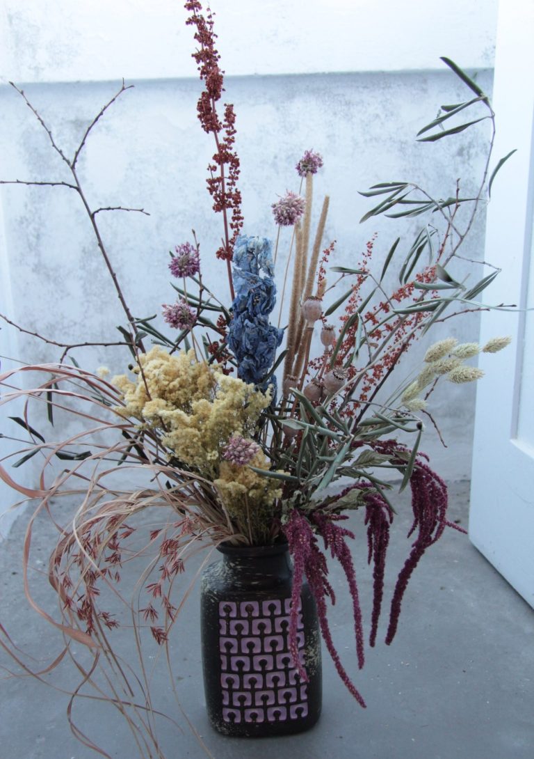 Heller Innenraum mit einem langen Tisch und grünen Hockern, dekoriert mit Trockenblumen.