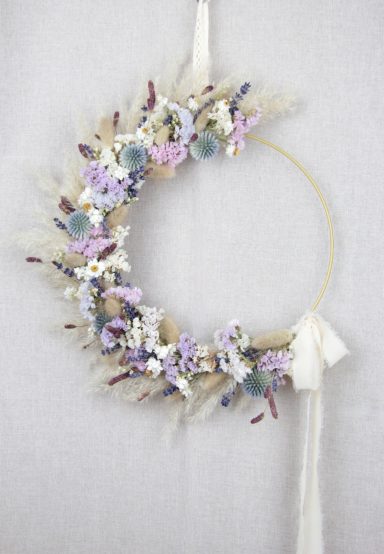 Blumenkranz mit lila, weißen und grünen Blumen an einem goldenen Ring.