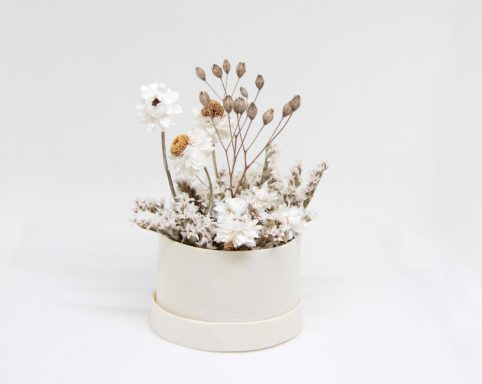 Weißer Topf mit getrockneten Blumen und Gräsern in sanften Brauntönen.