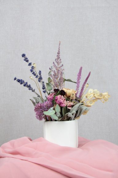 Bunte Trockenblumen in einer weißen Vase vor einem grauen Hintergrund.