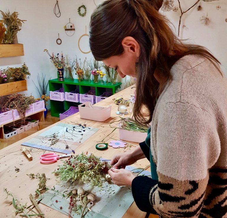 Frau bastelt mit getrockneten Blumen an einem Tisch, umgeben von Zubehör 