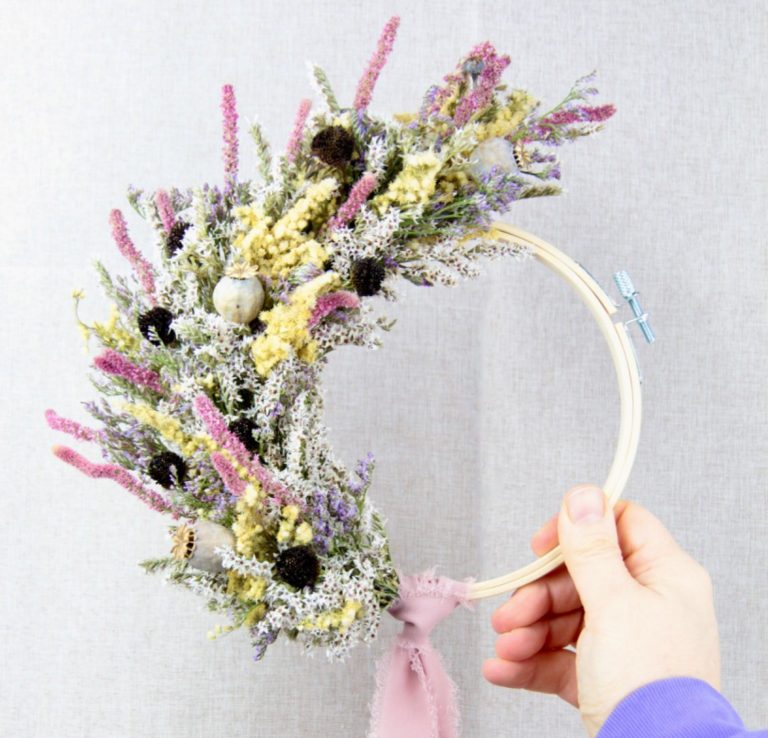 Hand haltend, Holzring mit getrockneten Blumen in lila und grün.