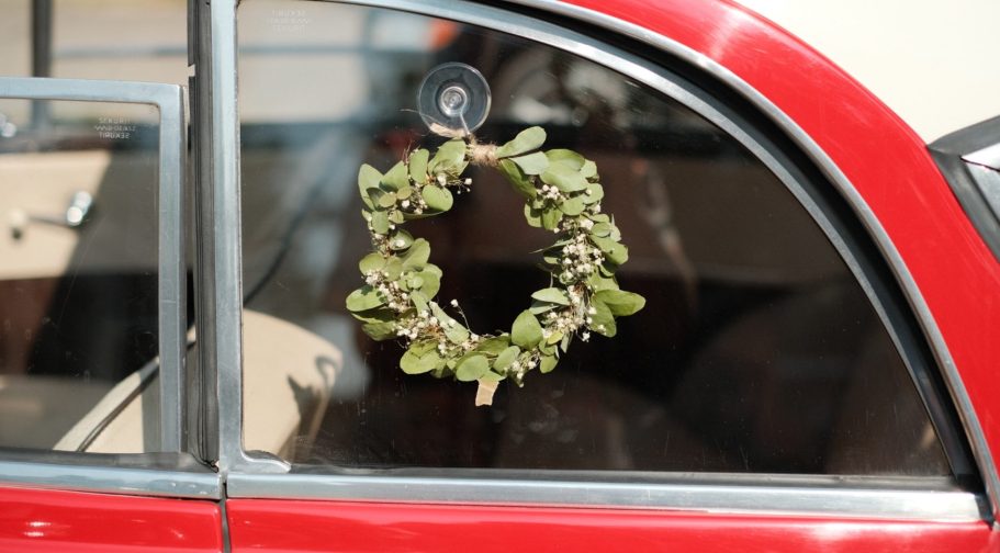 Kranz aus frischen Eukalyptus Blättern hängt an einem Roten Auto im Fenster.