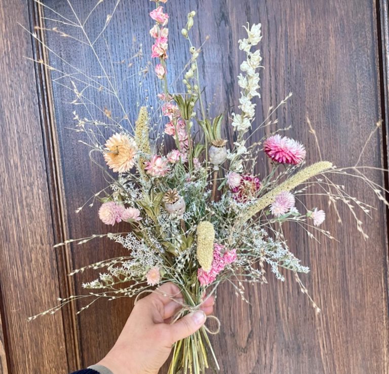 Hand aus Holz präsentiert einen Haarkranz aus Trockenblumen mit bunten Akzenten und Schleifen.