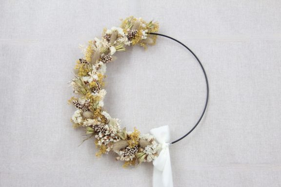 Ein runder Kranz aus getrockneten Blumen in sanften Farben mit einem weißen Band.