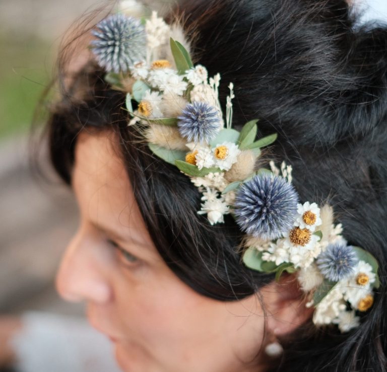 Hand aus Holz präsentiert einen Haarkranz aus Trockenblumen mit bunten Akzenten und Schleifen.