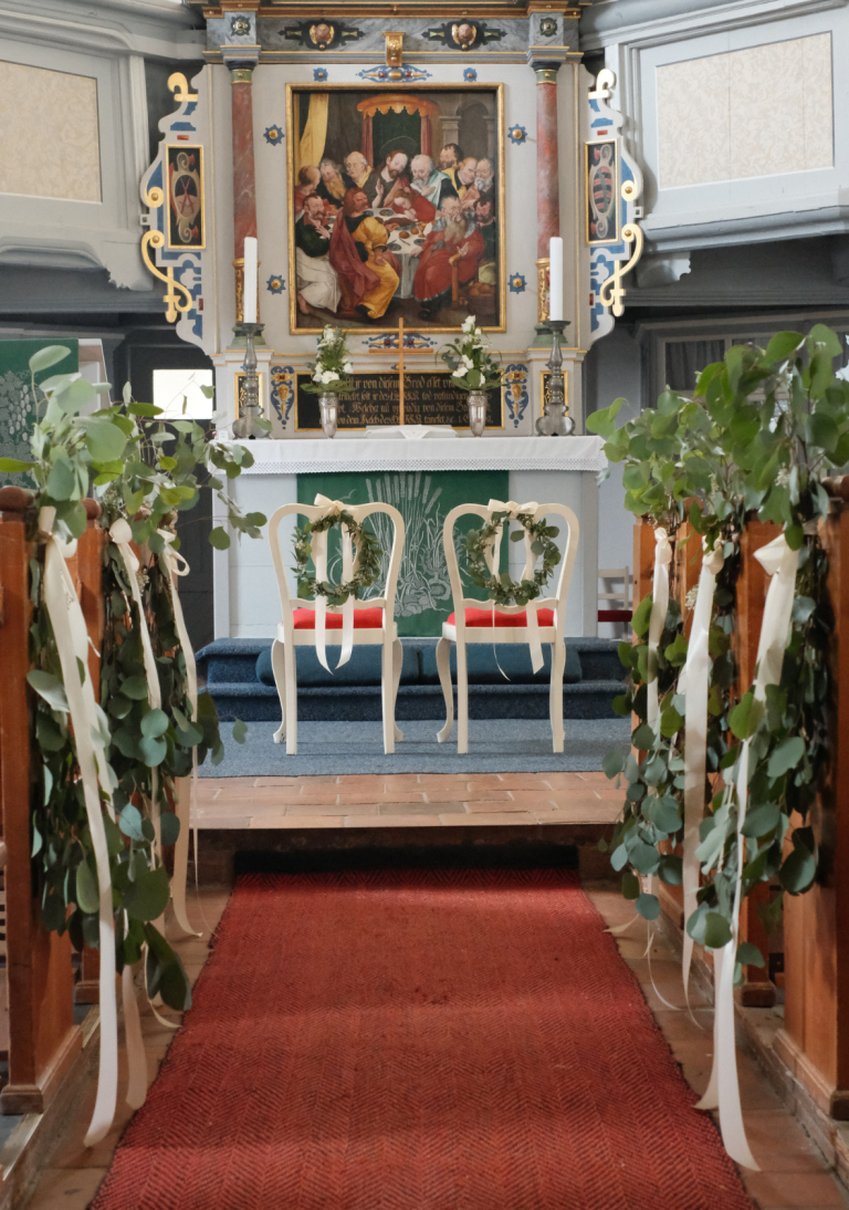 Bänke mit grünen Eukalyptuszweigen und dekorativen Bändern in einer Kirche geschmückt.