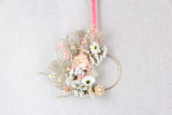 Dekorativer Kranz aus getrockneten Blumen in sanften Farben mit rosa Band.